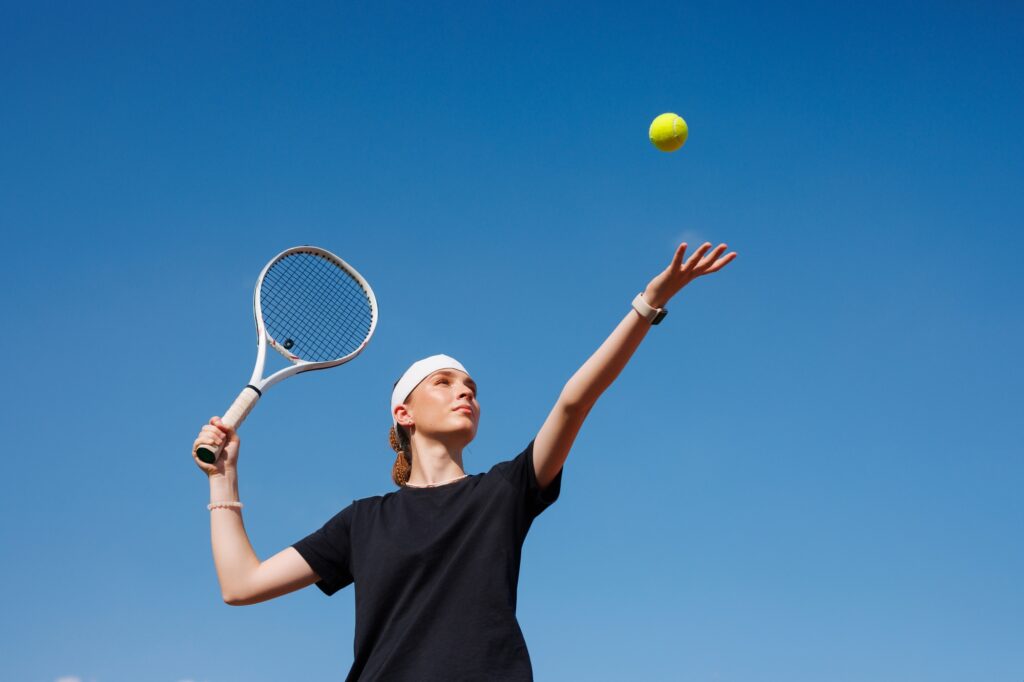 girl tennis player makes a hit with a tennis racket on a ball close-up on a sky background