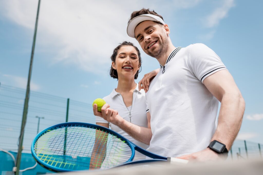 positive couple looking at camera, tennis racket and ball, summer activity, leisure and fun