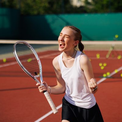 girl tennis player rejoices after scoring a goal, against the background of a tennis court