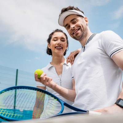 positive couple looking at camera, tennis racket and ball, summer activity, leisure and fun